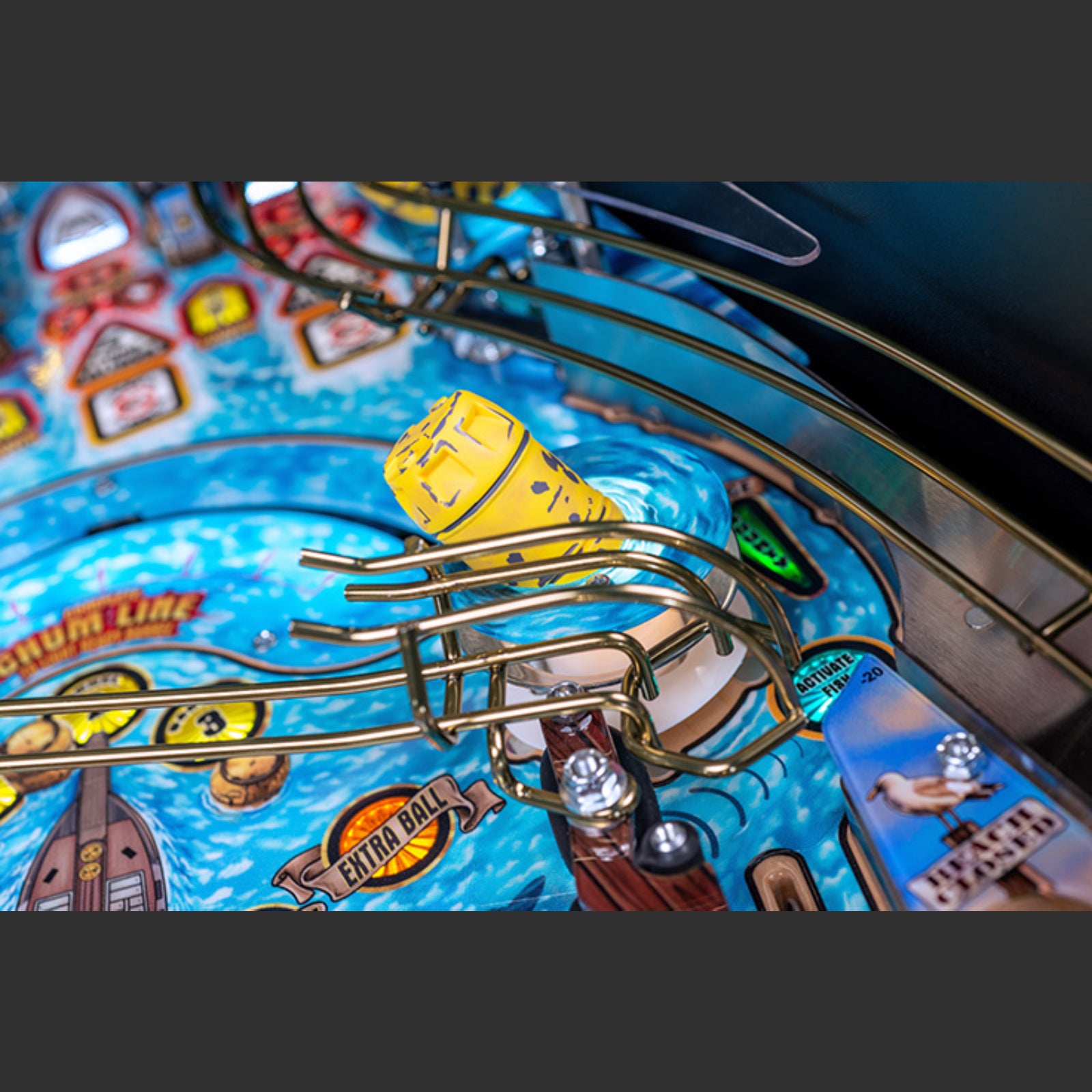 Nitro Pinball Sales Jaws 50th Annyversary Close-up of a pinball machine with a yellow ball on a blue playing field.
